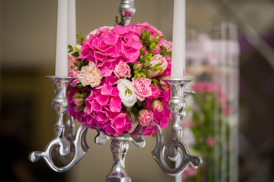 A floral arrangement featuring a bouquet of vibrant pink hydrangeas, soft pink roses, white lisianthus, and peach carnations, accented with green foliage, all nestled in a clear vase. The bouquet is p